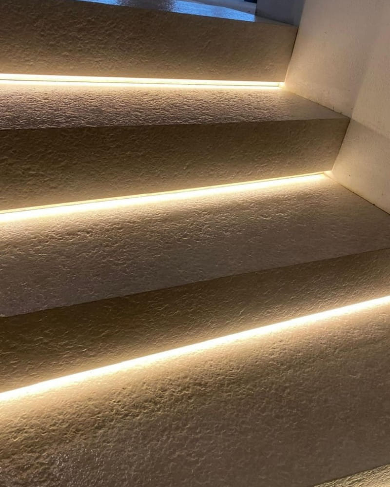 Detailaufnahme einer Treppe aus Naturstein mit integrierter LED-Beleuchtung an den Kanten jeder Stufe. Die Stufen haben eine raue, strukturierte Oberfläche, und das warme Licht sorgt für eine moderne und stilvolle Atmosphäre.